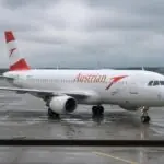 Επιβατικό αεροσκάφος της Austrian Airlines κινείται στον χώρο αεροδρομίου με συννεφιασμένο ουρανό.