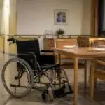 Άδειο αναπηρικό αμαξίδιο δίπλα σε τραπέζι τραπεζαρίας μονάδας φροντίδας ηλικιωμένων.