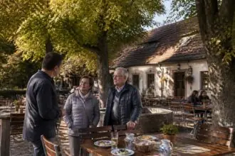 Συμβολική εικόνα παραδοσιακού Biergarten κάτω από φλαμουριές στη Φραγκονία, με εστιάτορα και επισκέπτες