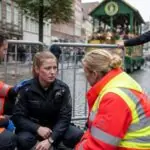 Συμβολική εικόνα από εορταστική παρέλαση στη Βρέμη, με δόκιμη αστυνομικό να δέχεται βοήθεια από διασώστες κοντά σε κιγκλιδώματα