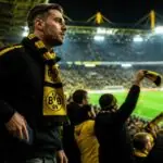 Οπαδός της Borussia Dortmund με κιτρινόμαυρο κασκόλ αφήνει το κινητό του στην άκρη στις εξέδρες γηπέδου