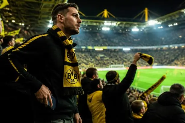 Οπαδός της Borussia Dortmund με κιτρινόμαυρο κασκόλ αφήνει το κινητό του στην άκρη στις εξέδρες γηπέδου