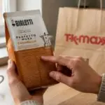 Χέρια καταναλωτή ελέγχουν συσκευασία αλεσμένου καφέ Bialetti με γεύση καραμέλα πάνω σε τραπέζι κουζίνας