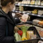 Καταναλωτής συγκρίνει συσκευασμένο έτοιμο γεύμα με υλικά μαγειρικής σε σούπερ μάρκετ.