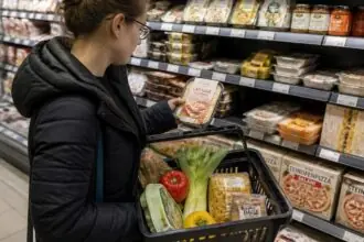 Καταναλωτής συγκρίνει συσκευασμένο έτοιμο γεύμα με υλικά μαγειρικής σε σούπερ μάρκετ.