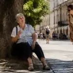 Ηλικιωμένη γυναίκα αναζητά σκιά σε ευρωπαϊκό δρόμο κατά τη διάρκεια έντονης ζέστης