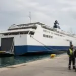 Eine Passagierfähre liegt an einem griechischen Hafen, während Hafenarbeiter am Kai stehen