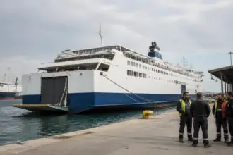 Eine Passagierfähre liegt an einem griechischen Hafen, während Hafenarbeiter am Kai stehen