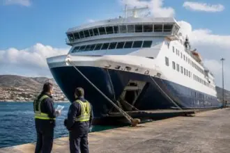 Große Passagierfähre am Kai eines griechischen Hafens mit zwei maritimen Beschäftigten im Vordergrund