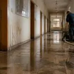Συμβολική εικόνα πλημμυρισμένου διαδρόμου γερμανικού σχολείου με νερό στο πάτωμα και κλειστές αίθουσες