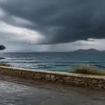 Regen und dunkle Gewitterwolken über einer griechischen Küstenstraße mit einer Person unter einem Regenschirm
