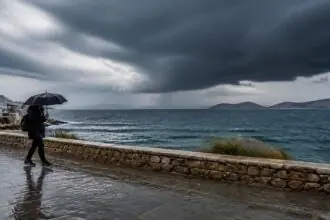 Regen und dunkle Gewitterwolken über einer griechischen Küstenstraße mit einer Person unter einem Regenschirm