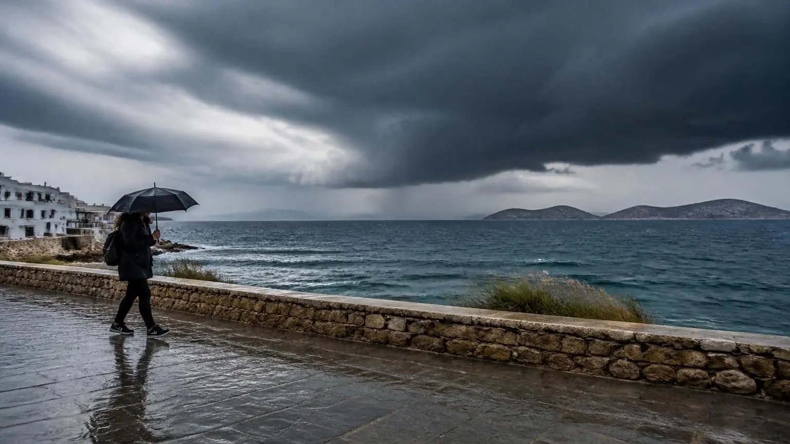 Regen und dunkle Gewitterwolken über einer griechischen Küstenstraße mit einer Person unter einem Regenschirm