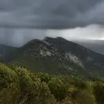 Dunkle Regenwolken über bewaldeten Bergen in einer griechischen Landschaft.