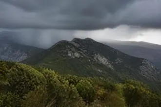Dunkle Regenwolken über bewaldeten Bergen in einer griechischen Landschaft.