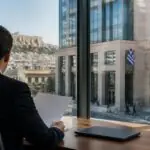 Symbolbild einer Bankfassade und eines Analysten bei der Auswertung von Unterlagen in Griechenland