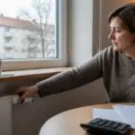 Κάτοικος διαμερίσματος στη Γερμανία ρυθμίζει τον θερμοστάτη καλοριφέρ δίπλα σε λογαριασμούς θέρμανσης.