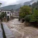 Schlammiges Hochwasser überflutet eine Dorfstraße in einer grünen griechischen Küstenlandschaft