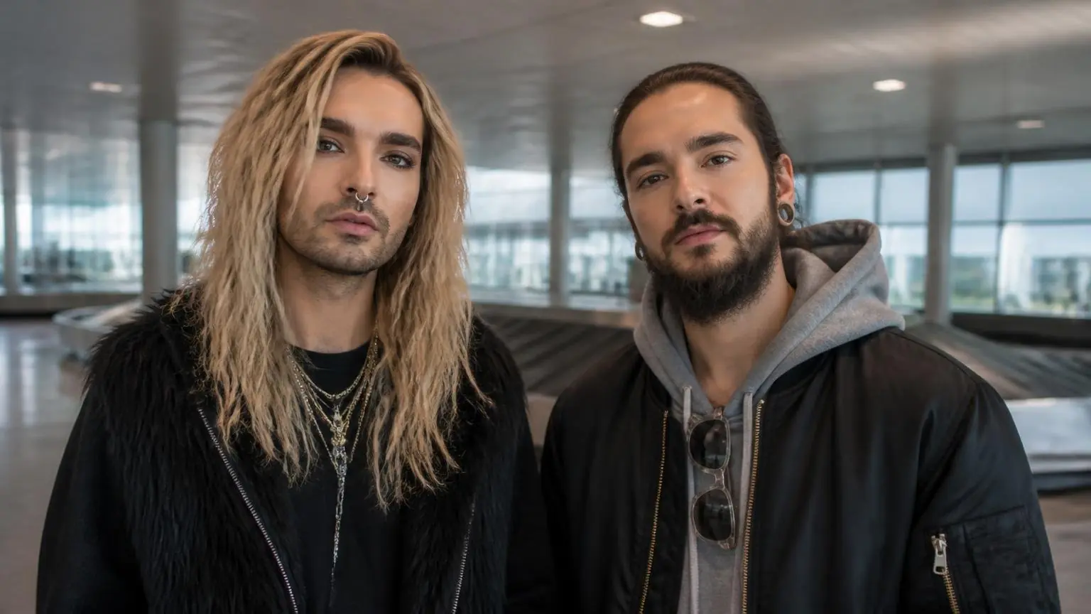 Οι Bill και Tom Kaulitz σε συμβολική απεικόνιση αεροδρομίου με άδειο ιμάντα αποσκευών