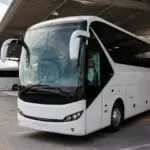 Ein weißer Reisebus steht an einem griechischen Busbahnhof, ein weiterer Bus ist im Hintergrund zu sehen.