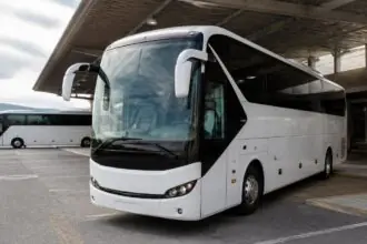 Ein weißer Reisebus steht an einem griechischen Busbahnhof, ein weiterer Bus ist im Hintergrund zu sehen.