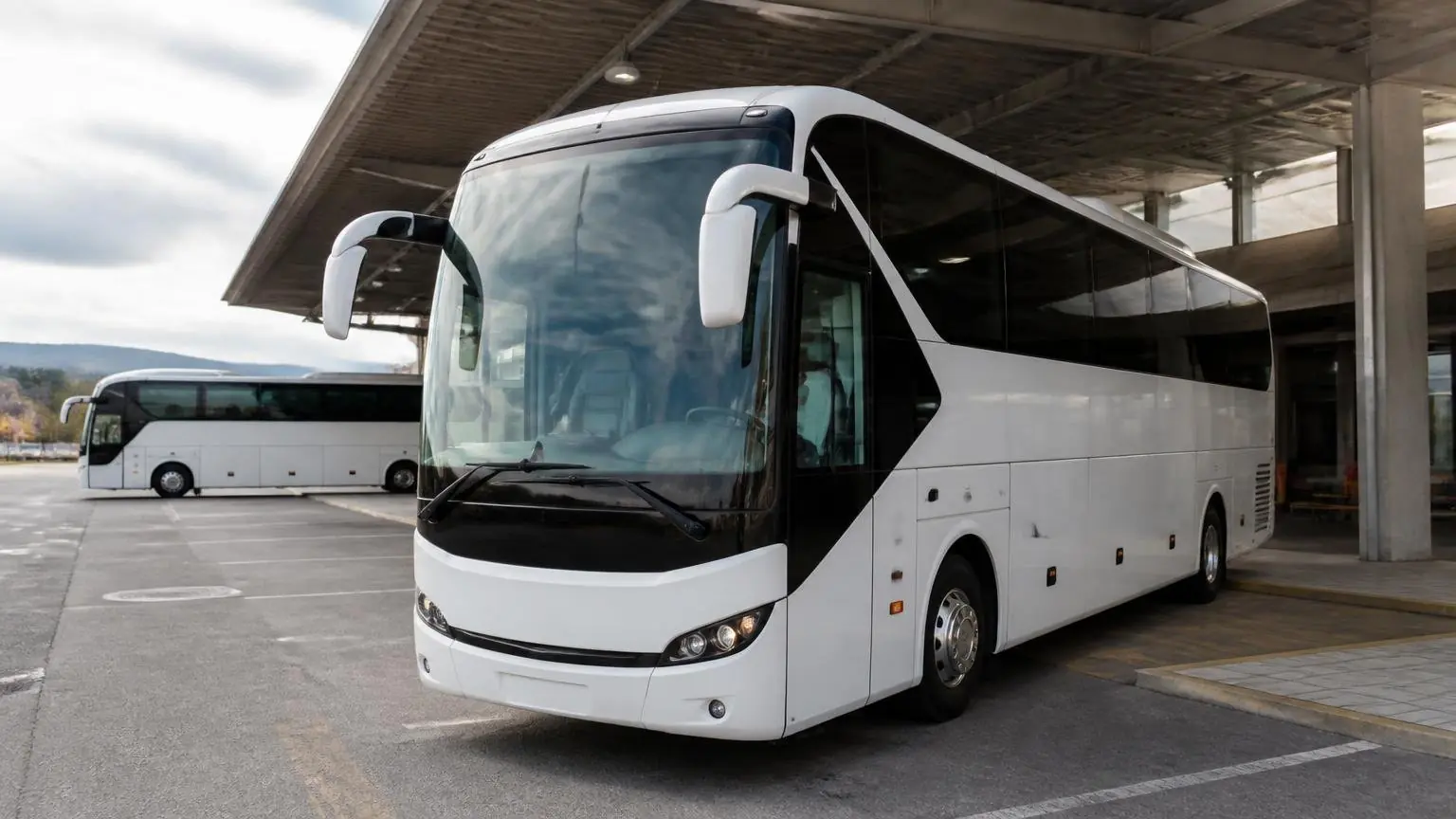 Ein weißer Reisebus steht an einem griechischen Busbahnhof, ein weiterer Bus ist im Hintergrund zu sehen.