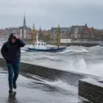 Ισχυροί άνεμοι και κύματα σε λιμάνι της Βόρειας Θάλασσας, με πεζούς να κινούνται στον παραλιακό δρόμο