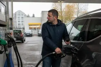 Οδηγός ανεφοδιάζει αυτοκίνητο σε πρατήριο καυσίμων στη Γερμανία και κοιτάζει την αντλία.