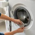 Πόρτα πλυντηρίου ρούχων μισάνοιχτη καθώς καθαρίζεται η ελαστική στεγανοποίηση μετά την πλύση