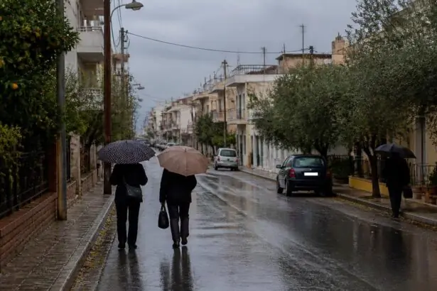 Regennasse Straße in einer griechischen Stadt mit Passanten unter Regenschirmen.