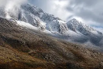 Symbolbild verschneiter Berggipfel über herbstlichen Hängen und Wolken auf Kreta