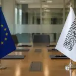 Σημαία της Ευρωπαϊκής Ένωσης απέναντι από λευκή σημαία των Ταλιμπάν σε συμβολικό χώρο συνομιλιών.