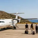 Reisende mit Gepäck neben einem Regionalflugzeug auf einem griechischen Inselflughafen, symbolische Darstellung