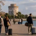 Symbolbild von Reisenden mit Koffern an der Uferpromenade von Thessaloniki mit dem Weißen Turm im Hintergrund