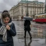 Πεζοί με ομπρέλες σε βροχερό δρόμο της Βιέννης, σε συμβολική εικόνα για το κύμα ψύχους