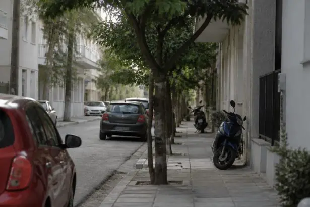 Wohnstraße in einer griechischen Stadt mit geparkten Autos und Motorrollern.