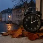 Συμβολική εικόνα ξυπνητηριού που δείχνει 02:00 ανάμεσα σε φθινοπωρινά φύλλα για την αλλαγή ώρας στη Γερμανία